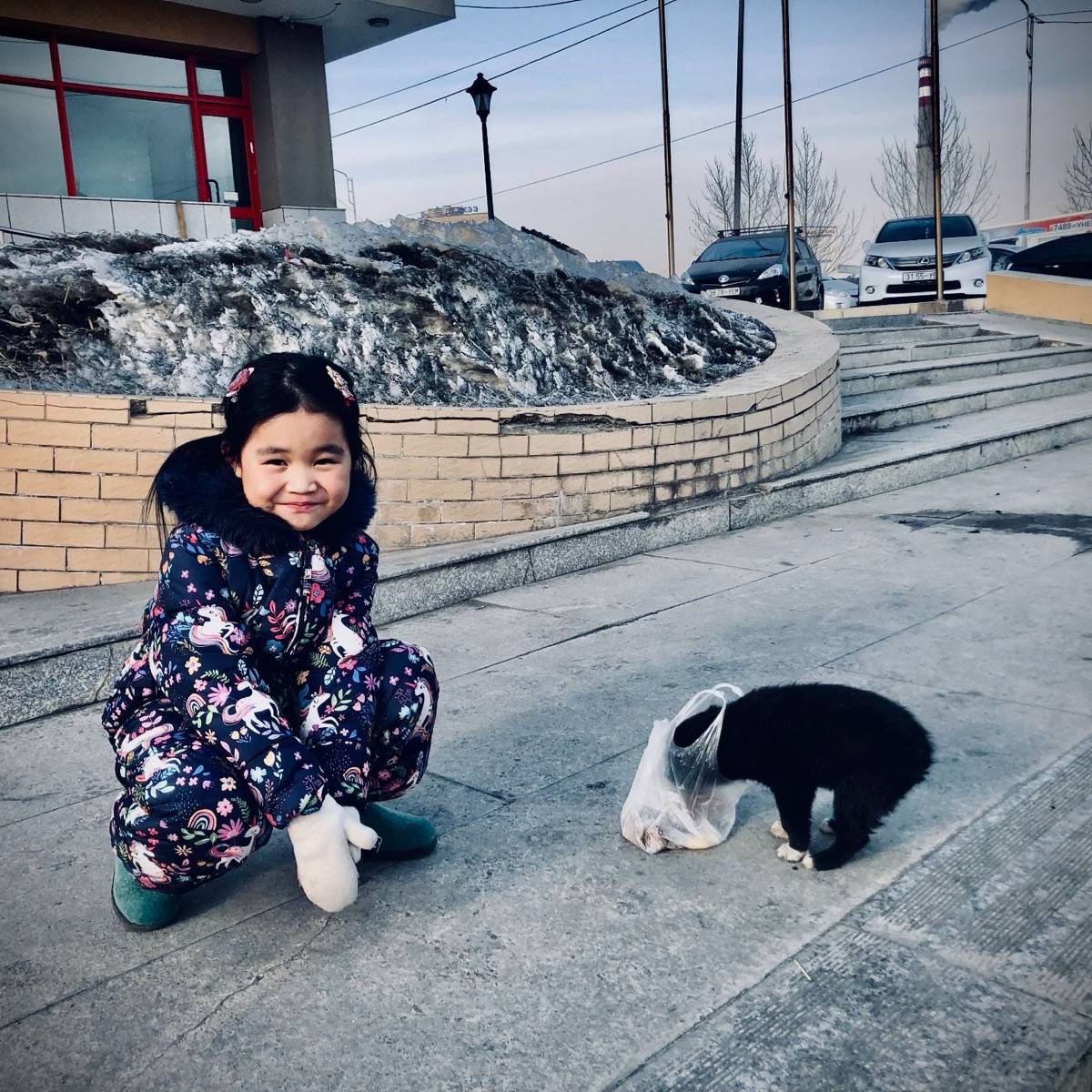 Lila smiling and kneeling beside a small dog on a snowy street in Ulaanbaatar